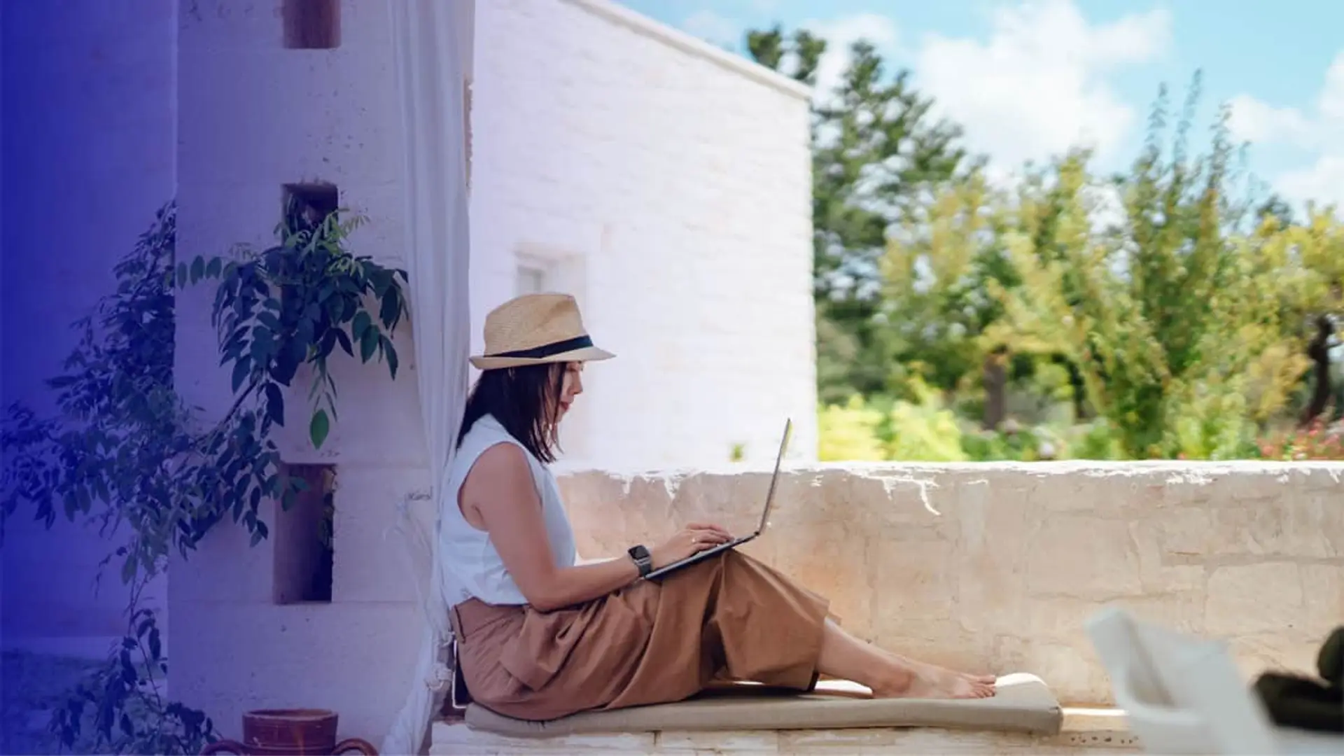 Quieres internet en tu segunda vivienda para Semana Santa: O2 te deja darte de baja sin penalización Mujer con sombrero trabajando con su portátil en una terraza para representar el teletrabajo y la conectividad móvil.