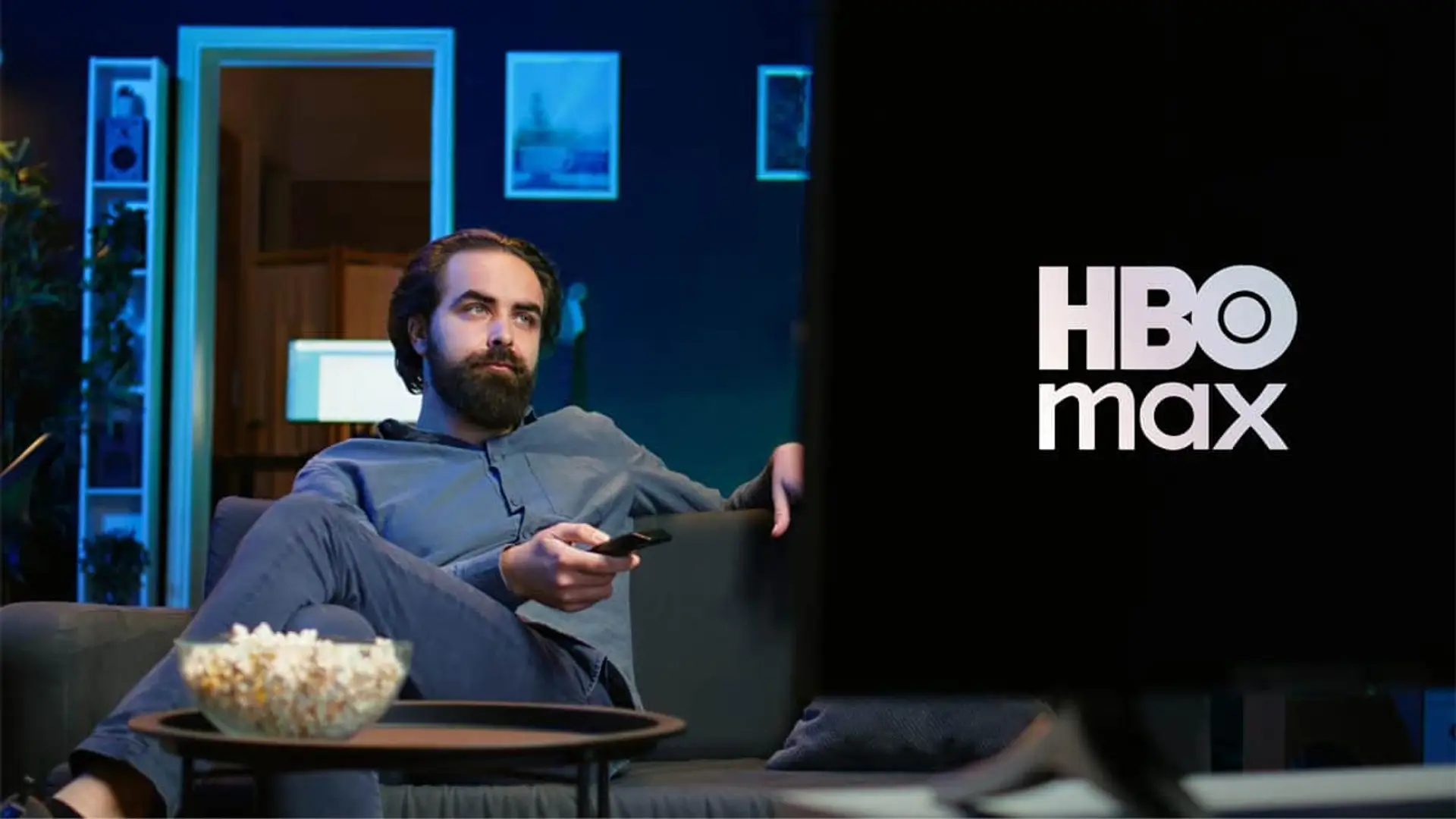 Hombre haciendo un maratón de series en HBO Max, relajado en el sofá de su casa por la noche con palomitas.