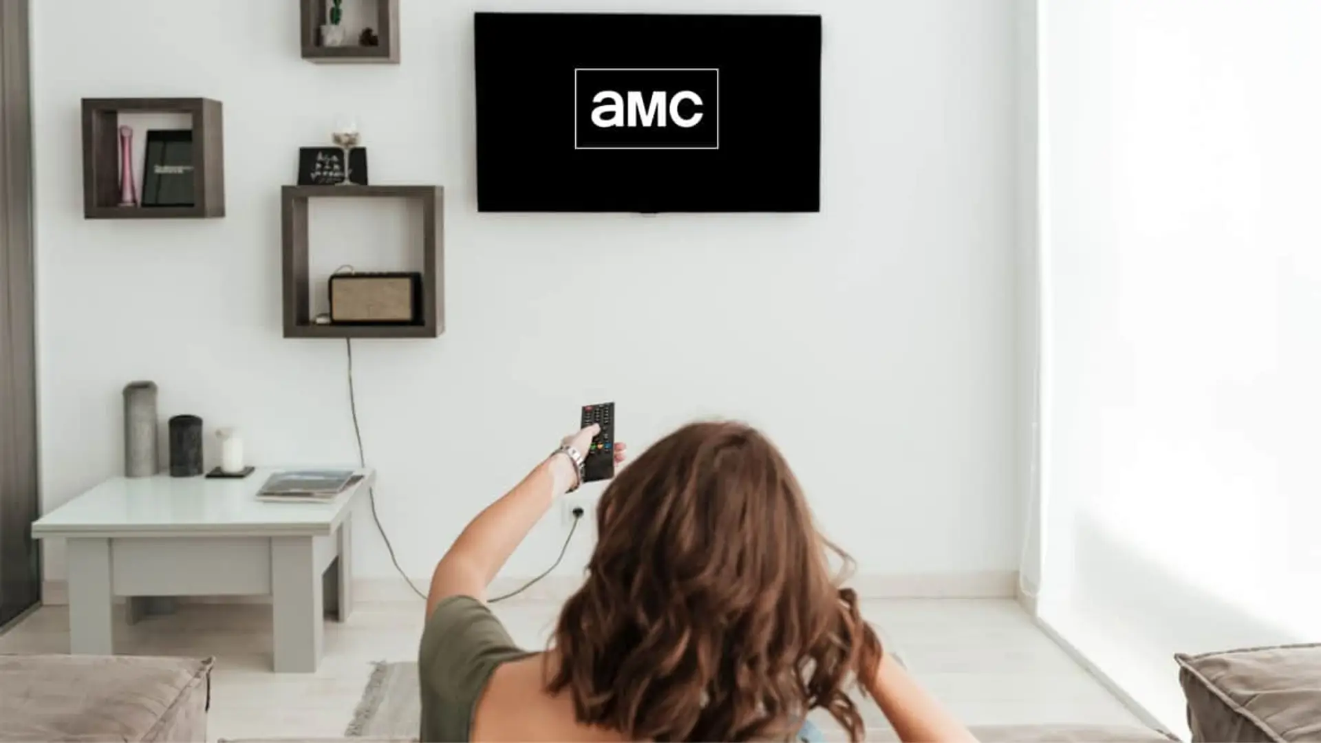 Mujer viendo el canal AMC en la televisión de su salón cambiando de canal con el mando.