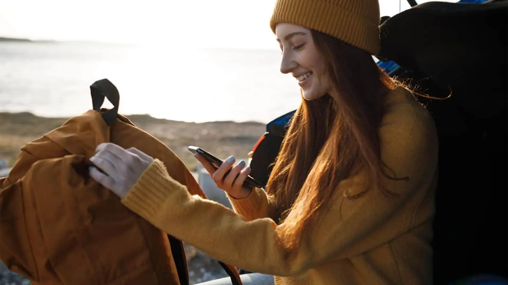 Mujer viajera consultando su smartphone junto a su mochila para usar una eSIM con datos en sus vacaciones.