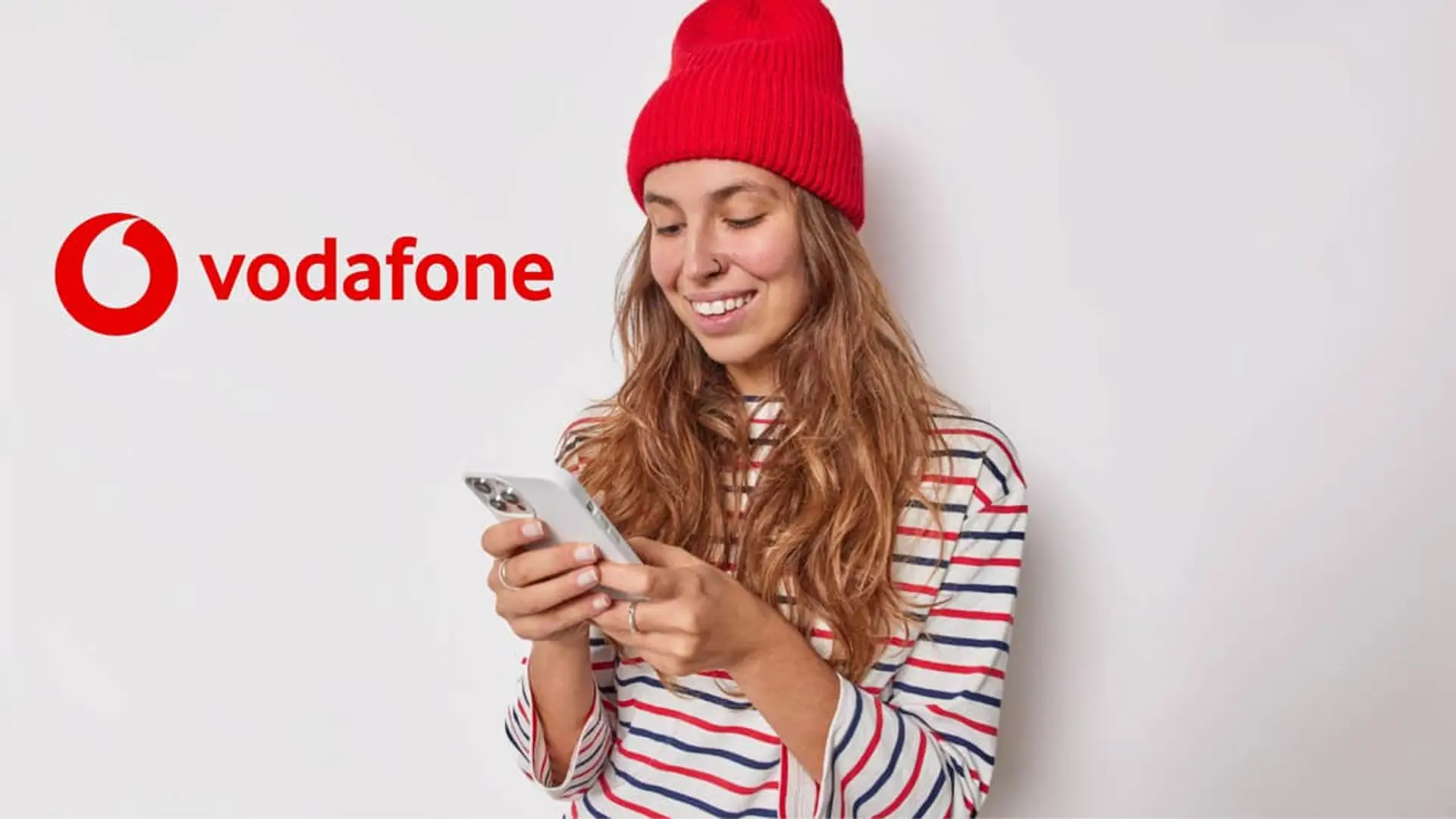 Mujer joven con smartphone junto al logo de Vodafone para promocionar sus tarifas de telefonía móvil y datos.