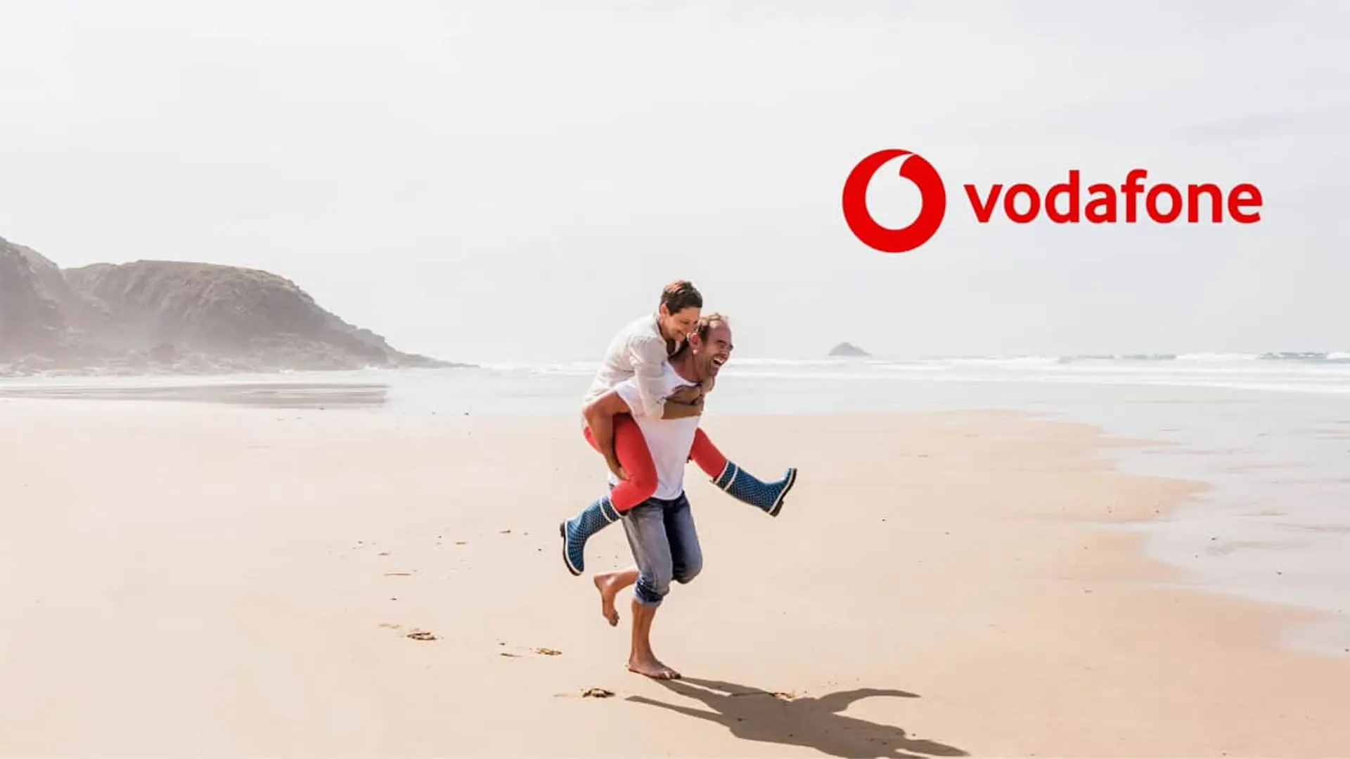 Pareja feliz en la playa junto al logo de Vodafone para representar la cobertura y servicios móviles durante las vacaciones.