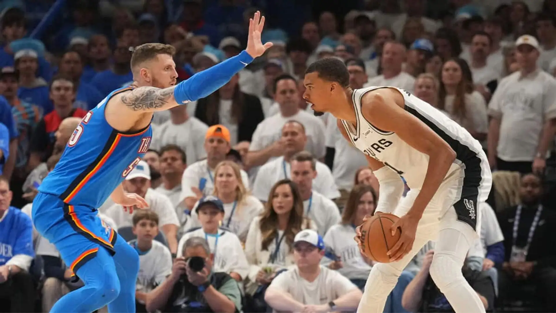 Dos jugadores de Oklahoma City Thunder y San Antonio Spurs de la NBA disputando una jugada durante un partido con el público al fondo