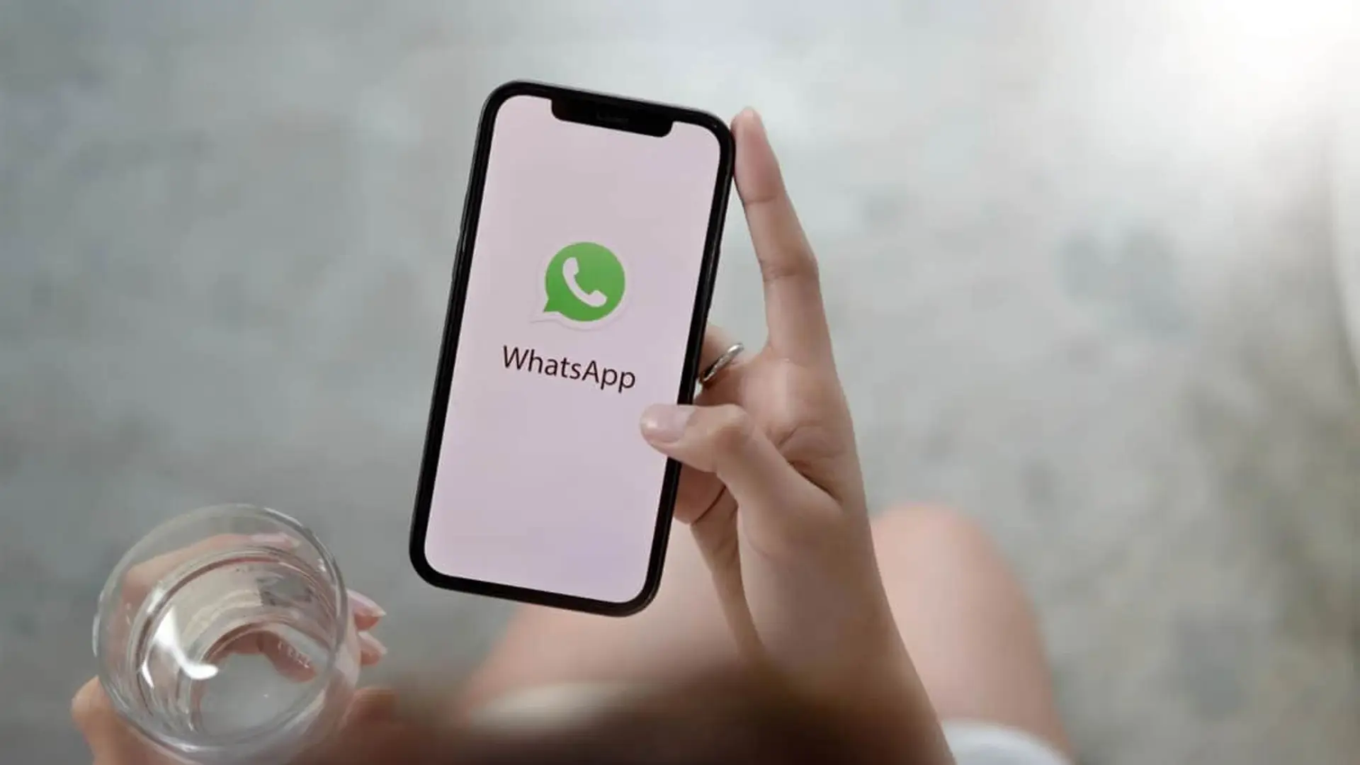 Mano sosteniendo un smartphone con el logotipo de WhatsApp en pantalla para mensajería instantánea.