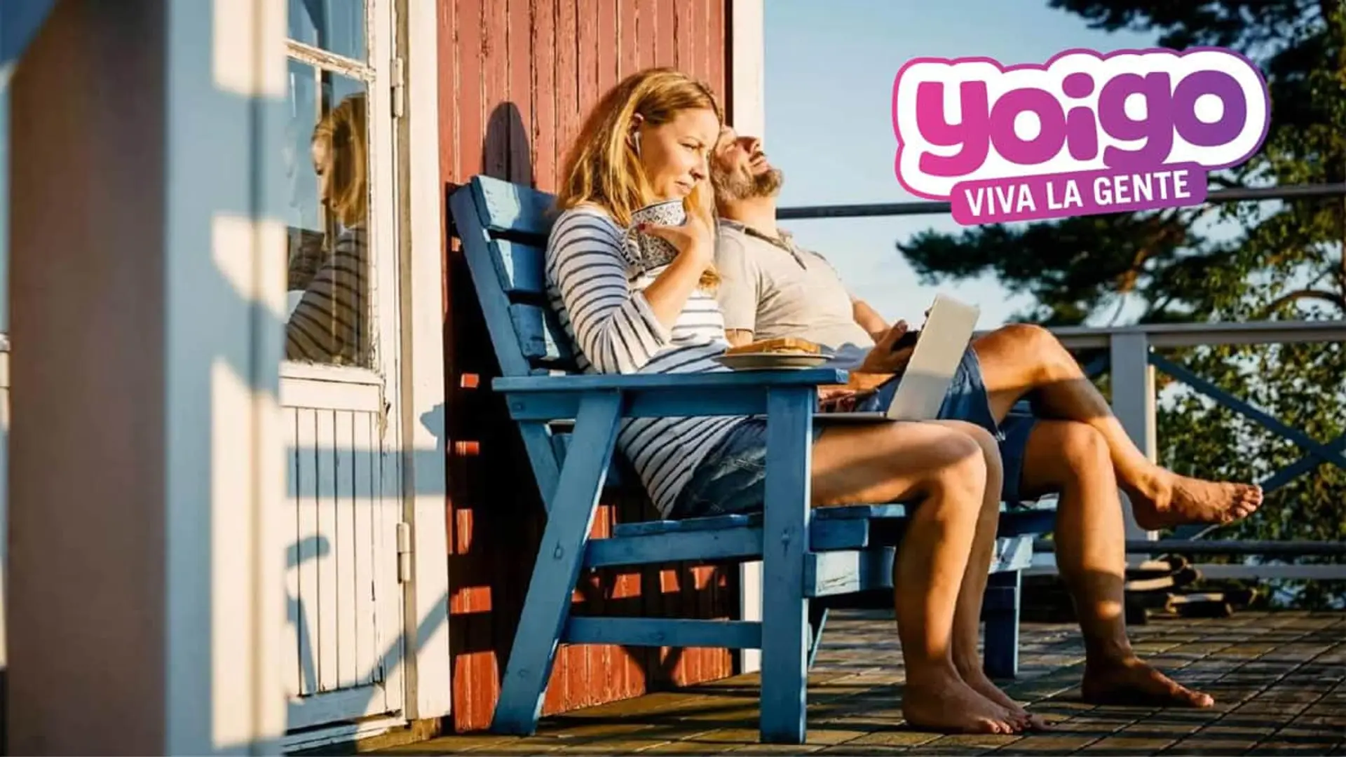 Pareja usando un portátil en la terraza con el logotipo de Yoigo para servicios de internet en segunda residencia.