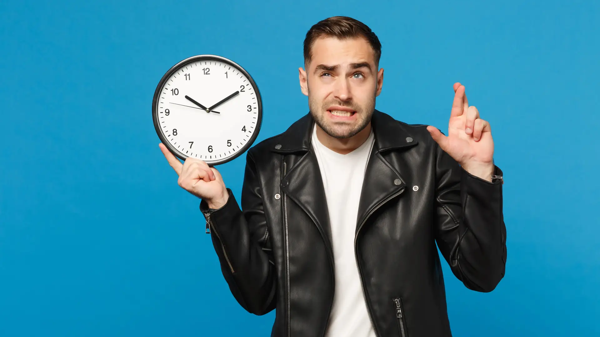 Hombre joven con cazadora negra sujeta un reloj mientras cruza los dedos para que se termine la permanencia de su contrato adamo cuanto antes Hombre joven con cazadora negra sujeta un reloj mientras cruza los dedos para que se termine la permanencia de su contrato adamo cuanto antes