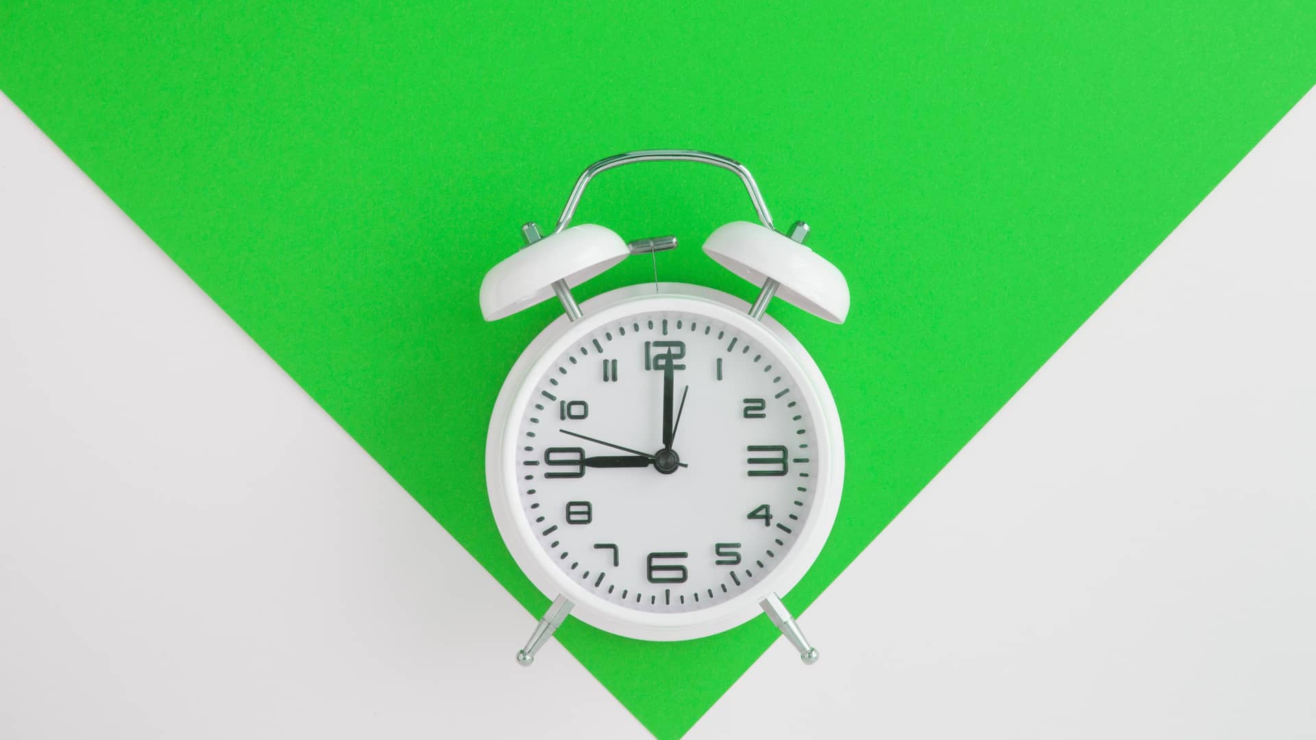 Reloj despertador blanco sobre fondo verde representa la permanencia de algunas tarifas amena