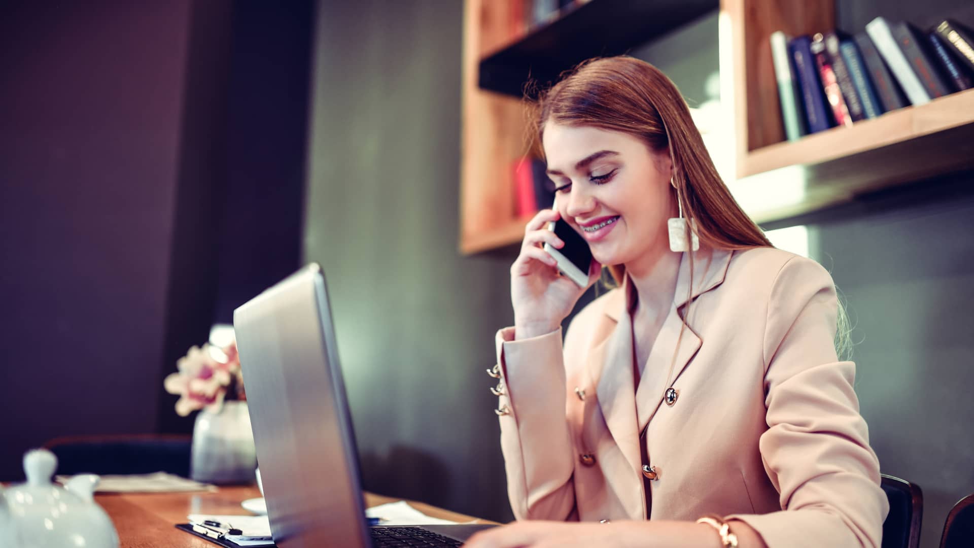 Joven recepcionista habla por teléfono en el trabajo mientras trabaja en su portátil gracias a la tarifa de Avatel de su móvil de empresa