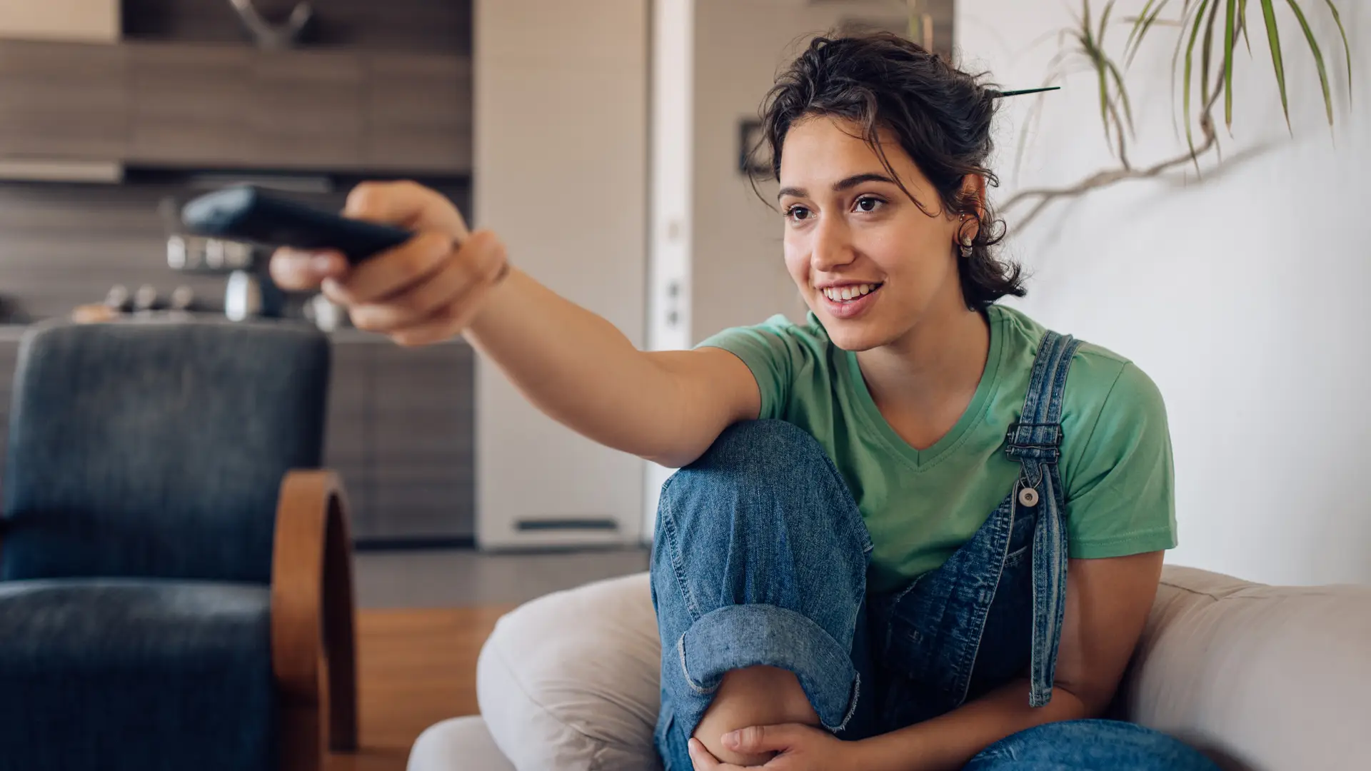 Mujer con peto vaquero sonrie mientras escoge zappea en su tele gracias a su tarifa de tv de Avatel Mujer con peto vaquero sonrie mientras escoge zappea en su tele gracias a su tarifa de tv de Avatel
