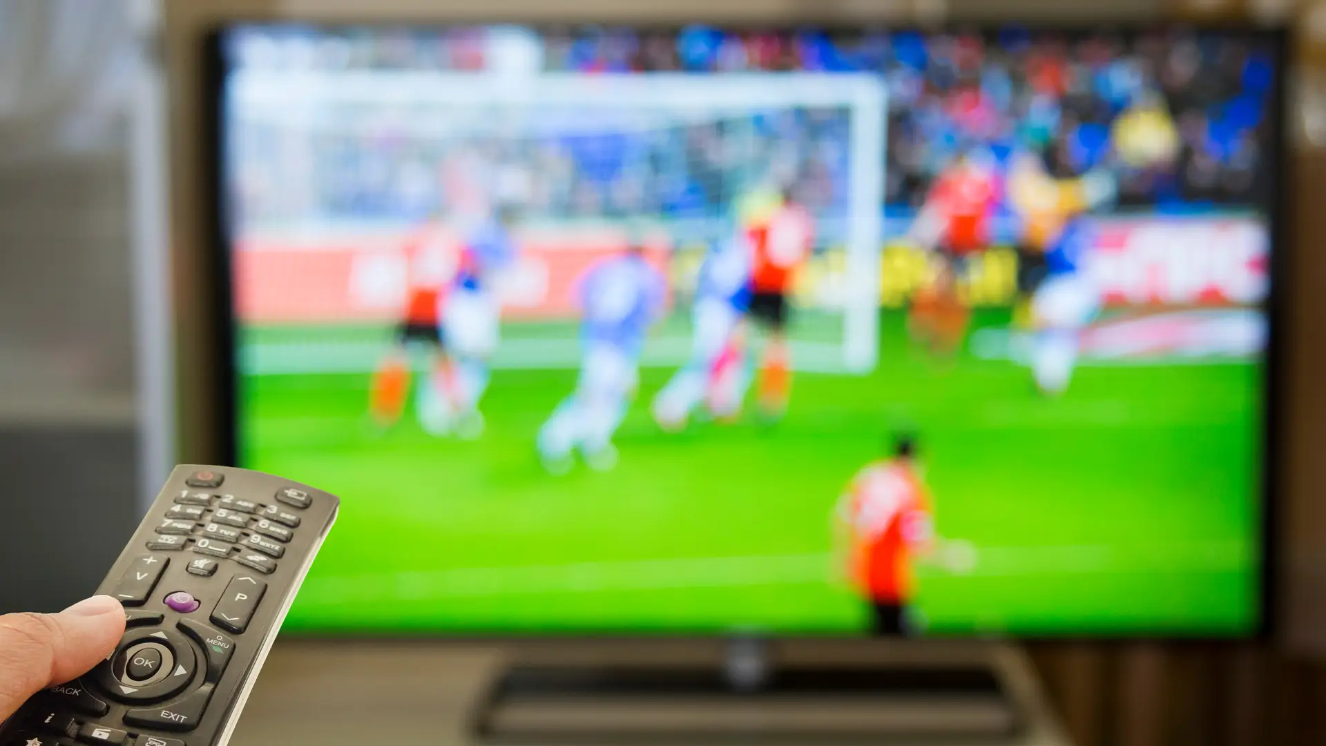 Joven con mando a distancia viendo partido de fútbol en la televisión Joven con mando a distancia viendo partido de fútbol en la televisión