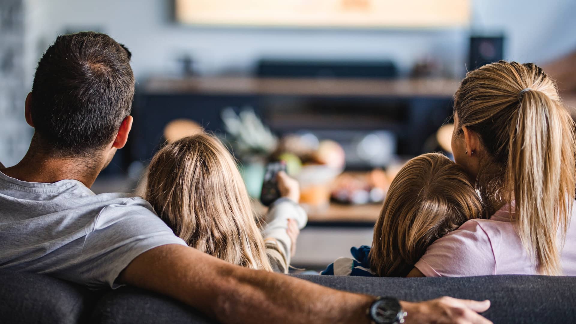 Vista trasera de una familia viendo la televisión en el sofá en casa simboliza tarifas móvil internet tv familia