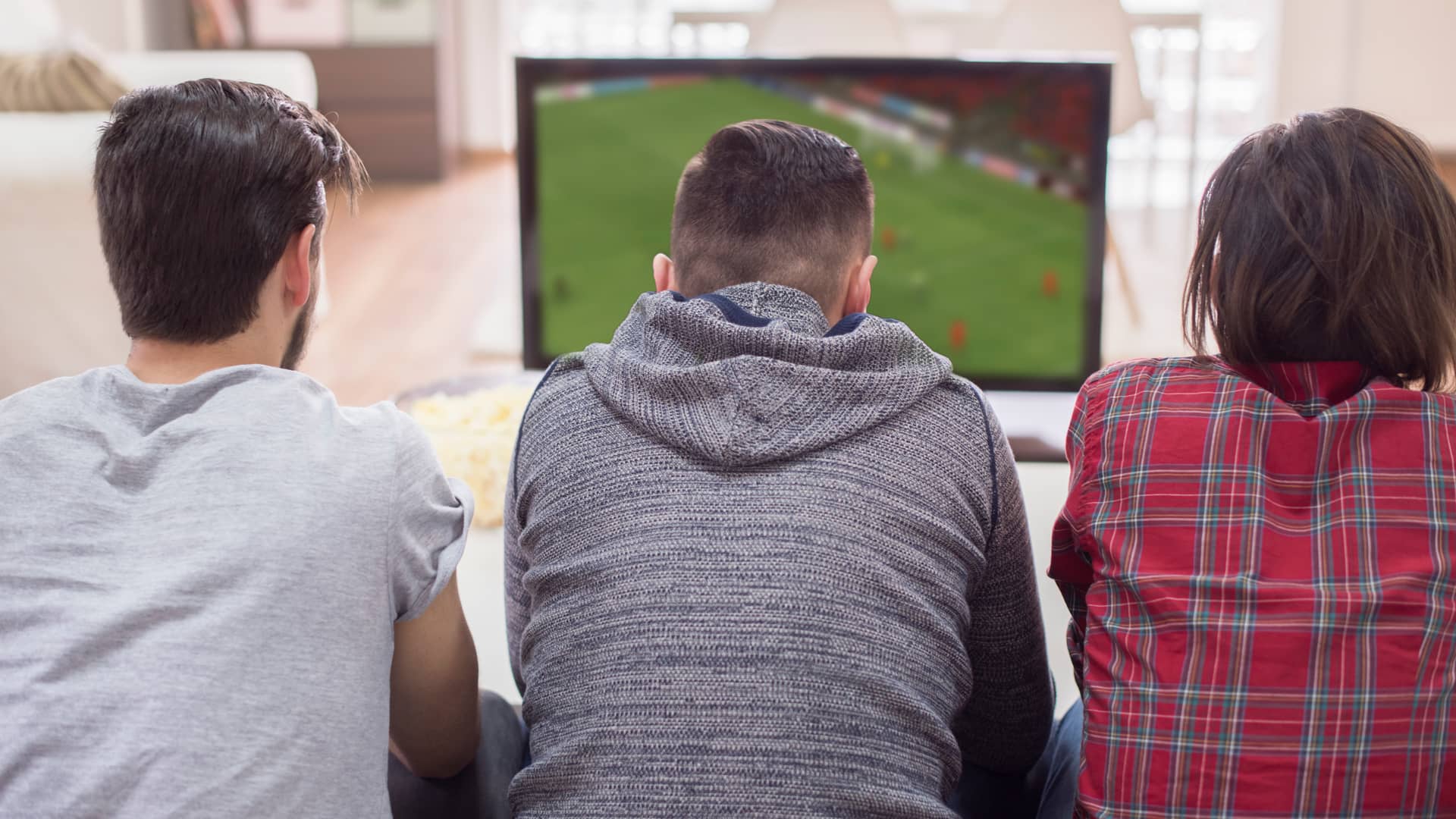 Tres amigos disfrutan de un partido de fútbol en su televisión a través de finetwork tras consultar nuestra guía