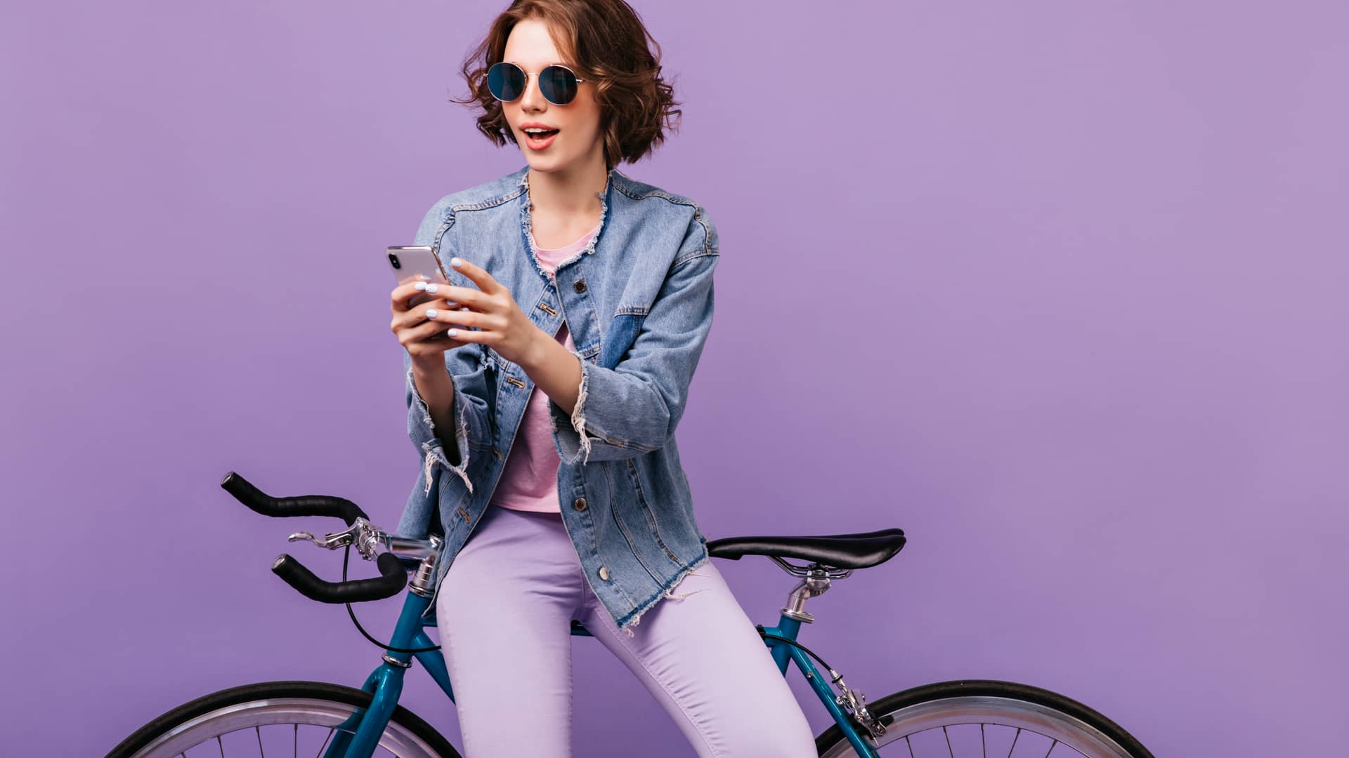 Mujer vestida de morado apoyada en su bicicleta aprovecha para revisar mensajes en su teléfono