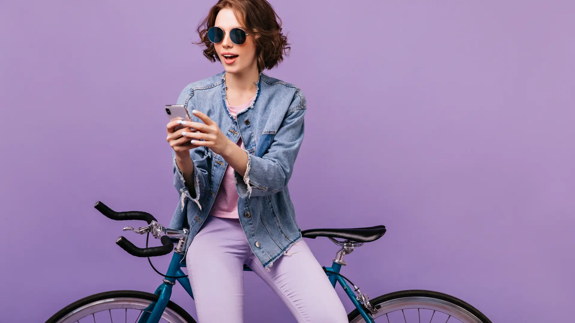 Mujer vestida de morado apoyada en su bicicleta aprovecha para revisar mensajes en su teléfono Mujer vestida de morado apoyada en su bicicleta aprovecha para revisar mensajes en su teléfono