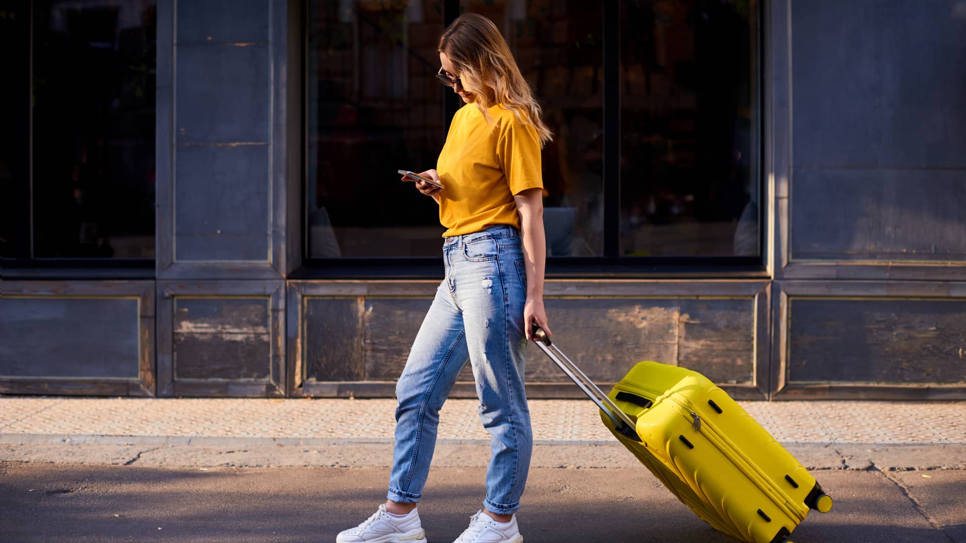 Joven con camiseta.y maleta amarillas utiliza su smartphone tras haber consultado previamente las condiciones de roaming de su contrato jazztel