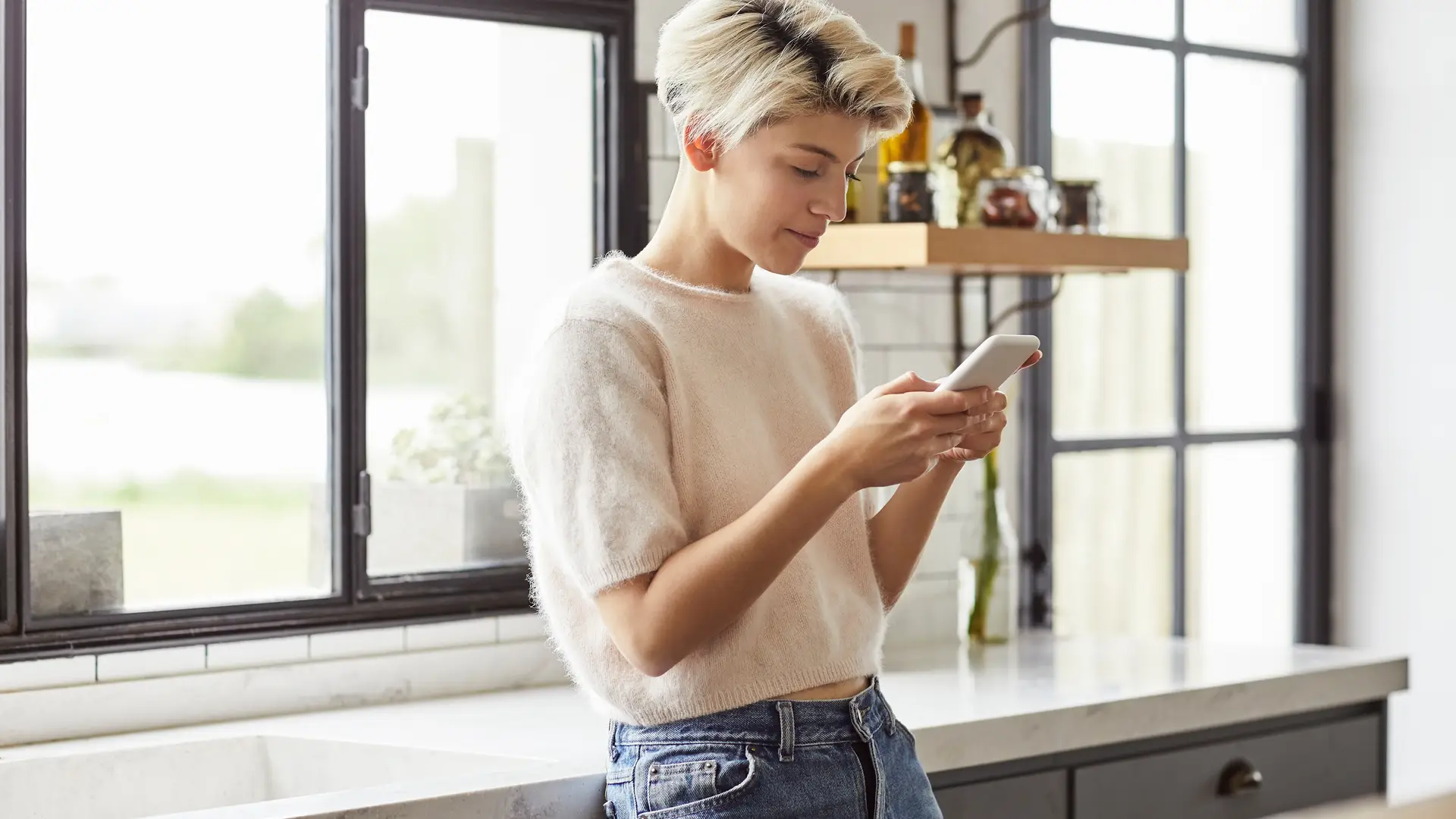 Mujer en la cocina con su smartphone viendo cuales son los trámites para activar sim llamaya Mujer en la cocina con su smartphone viendo cuales son los trámites para activar sim llamaya