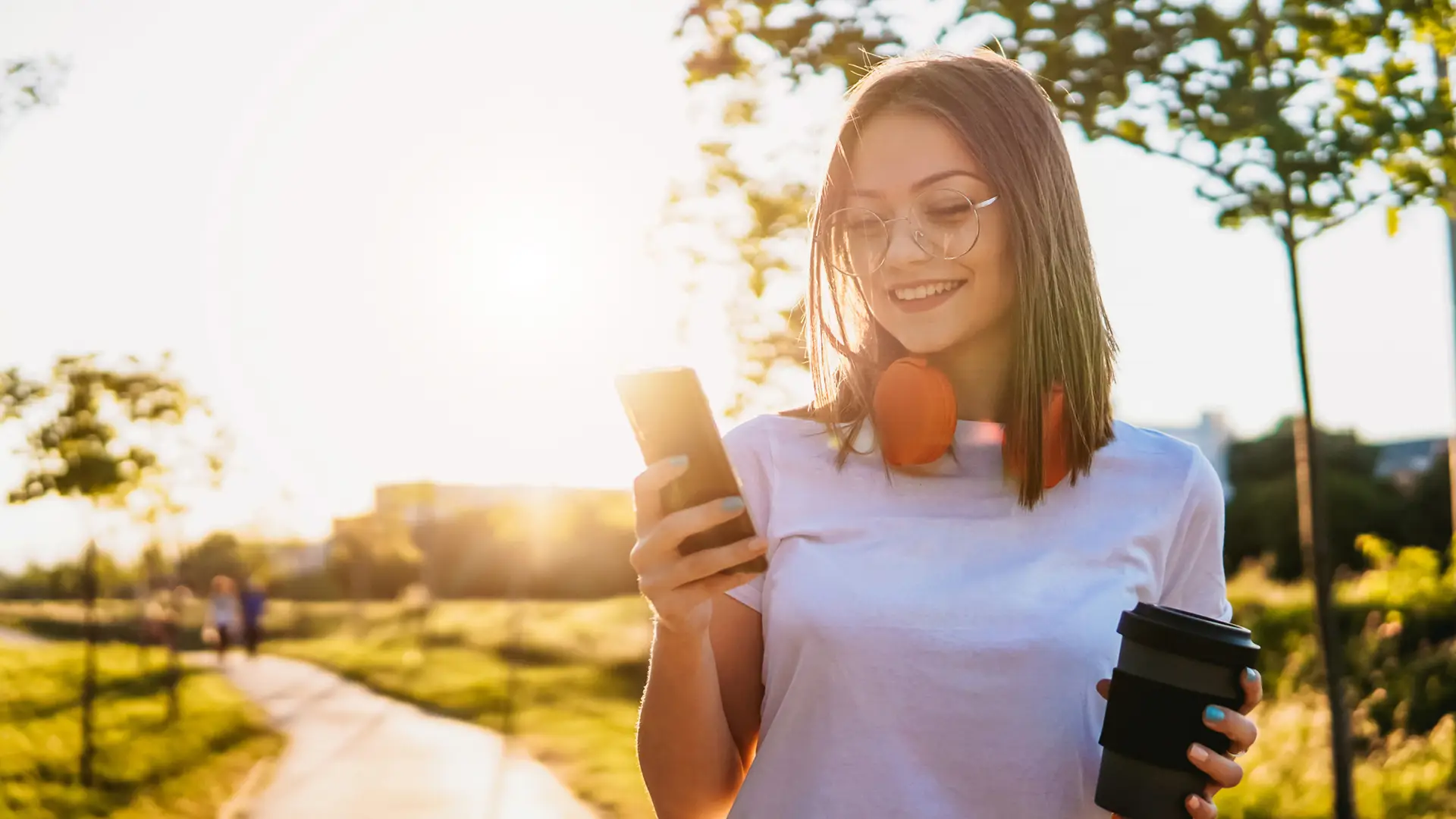 Mujer paseando y tomando un café mientras busca en su smartphone los códigos ussd de másmovil Mujer paseando y tomando un café mientras busca en su smartphone los códigos ussd de másmovil