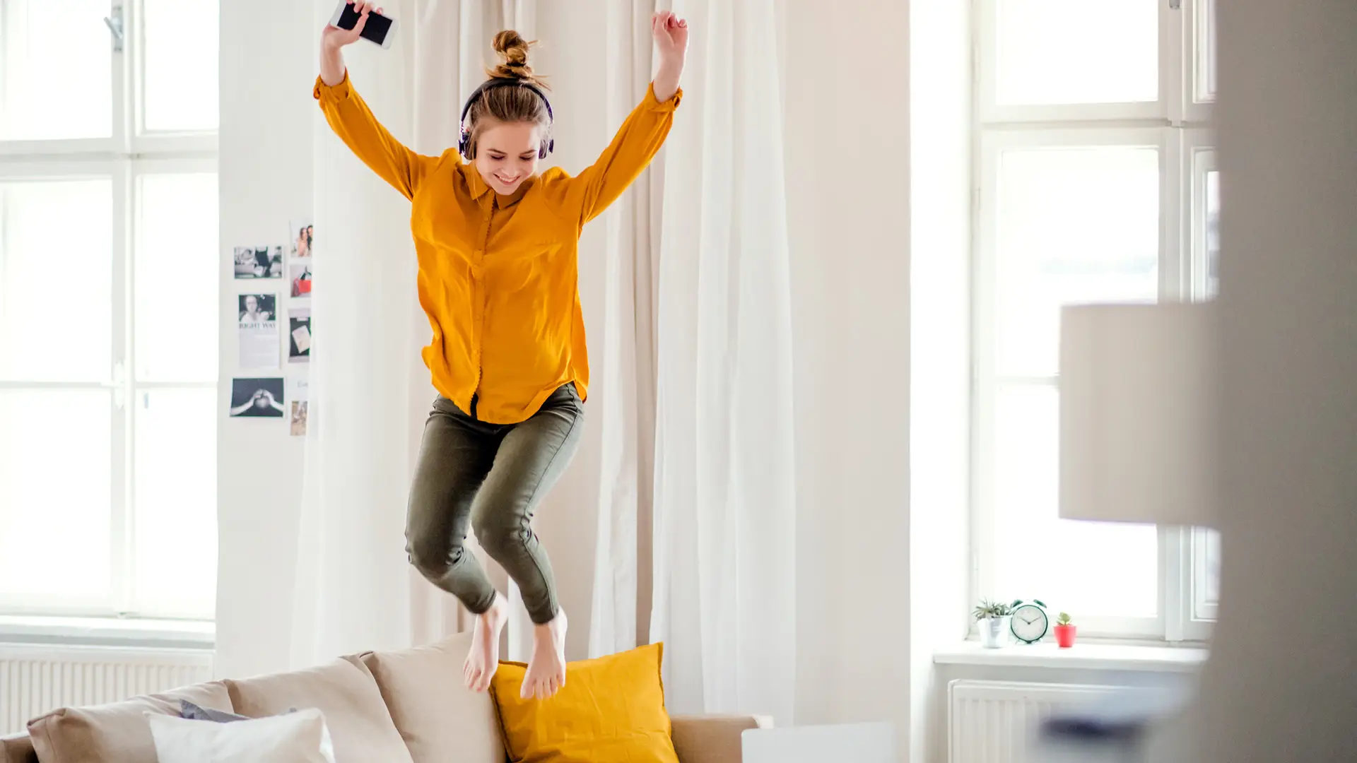 Una joven estudiante con auriculares saltando en el sofá simboliza portabilidad másmovil Una joven estudiante con auriculares saltando en el sofá simboliza portabilidad másmovil
