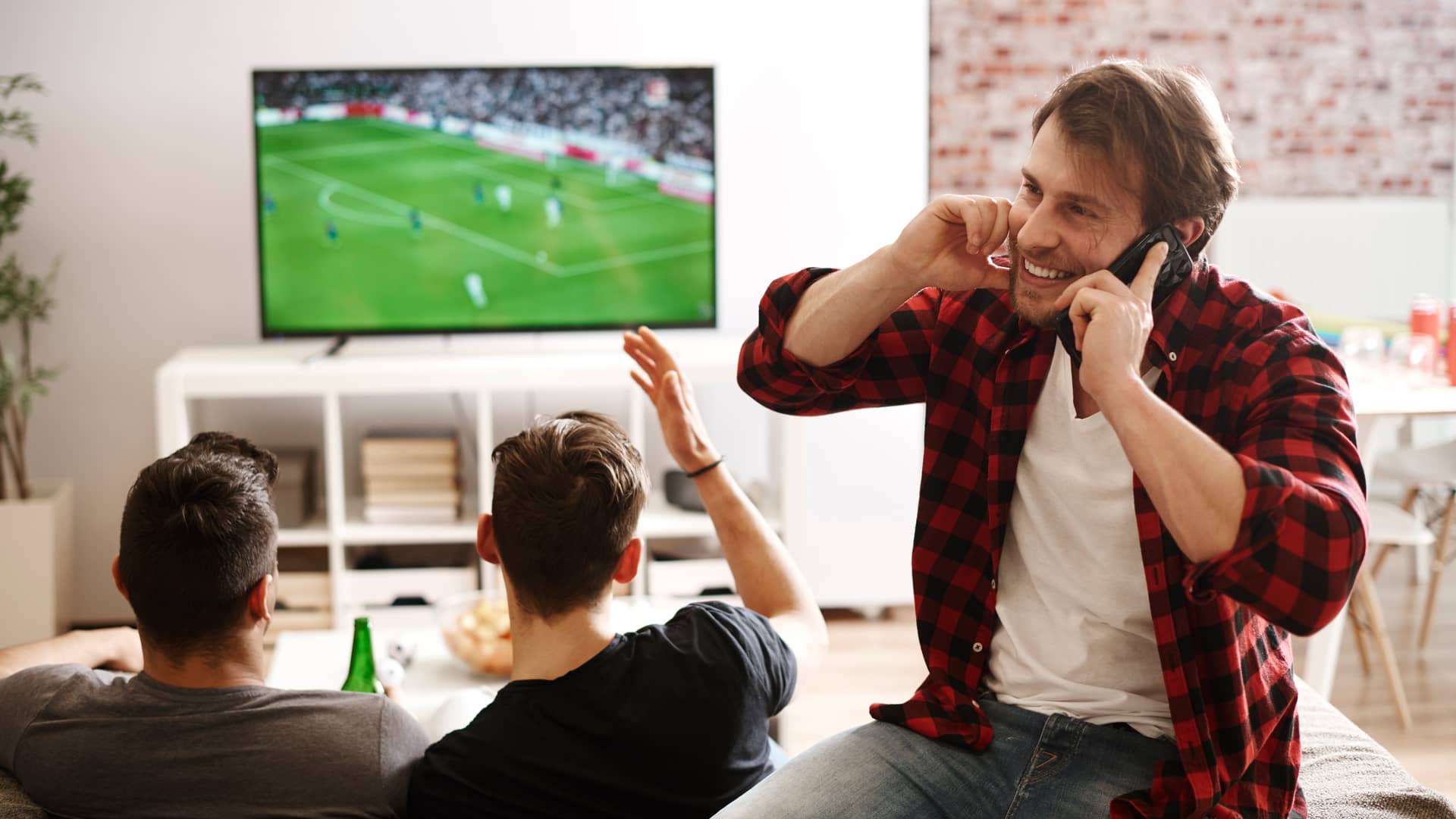 Hombre recibe una llamada mientras sus amigos disfrutan de La Liga en televisión gracias a su contrato Movistar