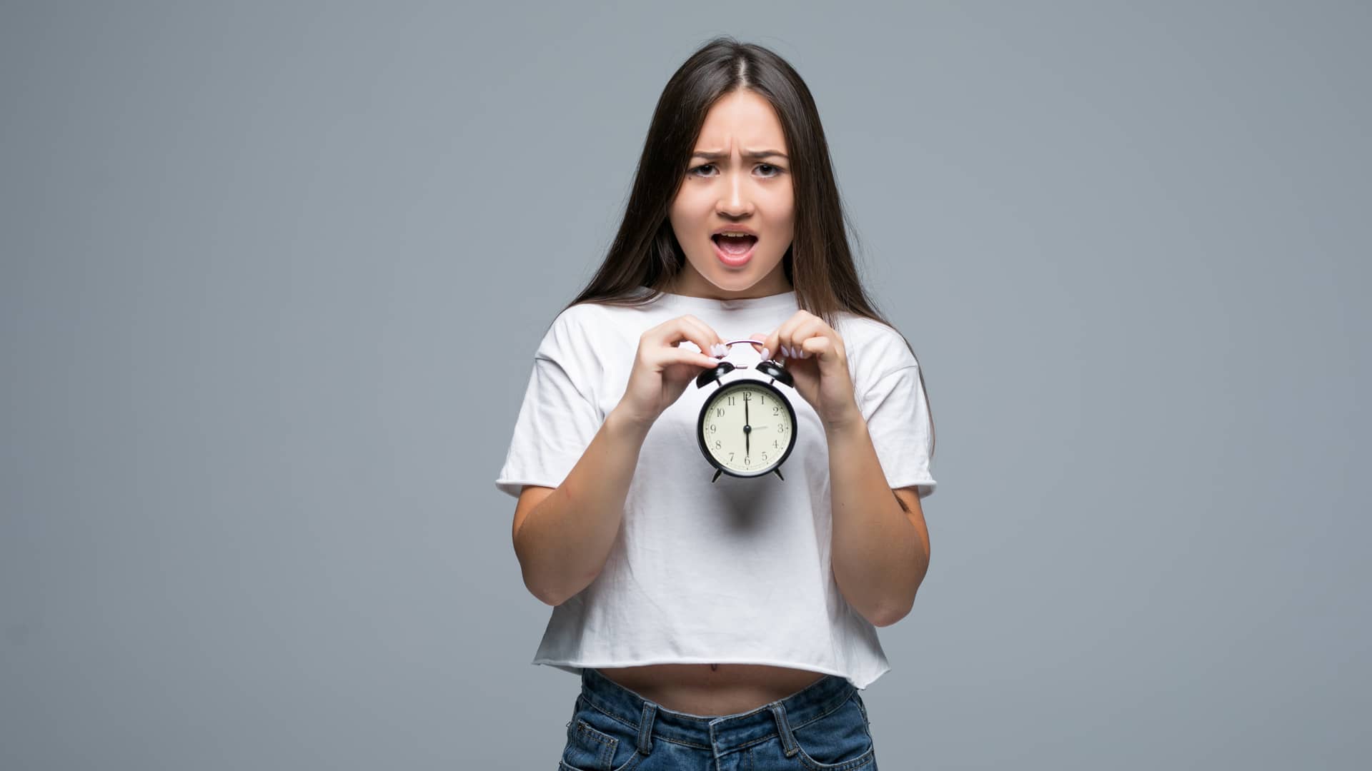 Mujer joven con cara de enfado sujeta un reloj que simboliza la permanencia de su tarifa R