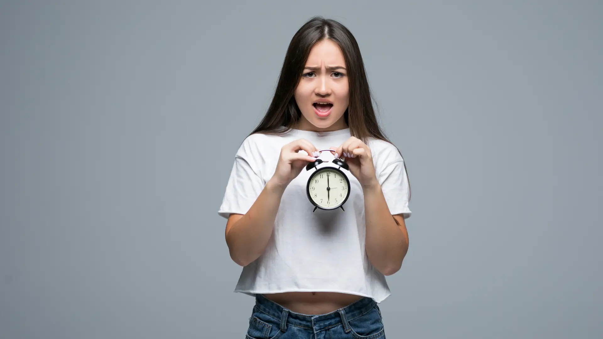 Mujer joven con cara de enfado sujeta un reloj que simboliza la permanencia de su tarifa R Mujer joven con cara de enfado sujeta un reloj que simboliza la permanencia de su tarifa R