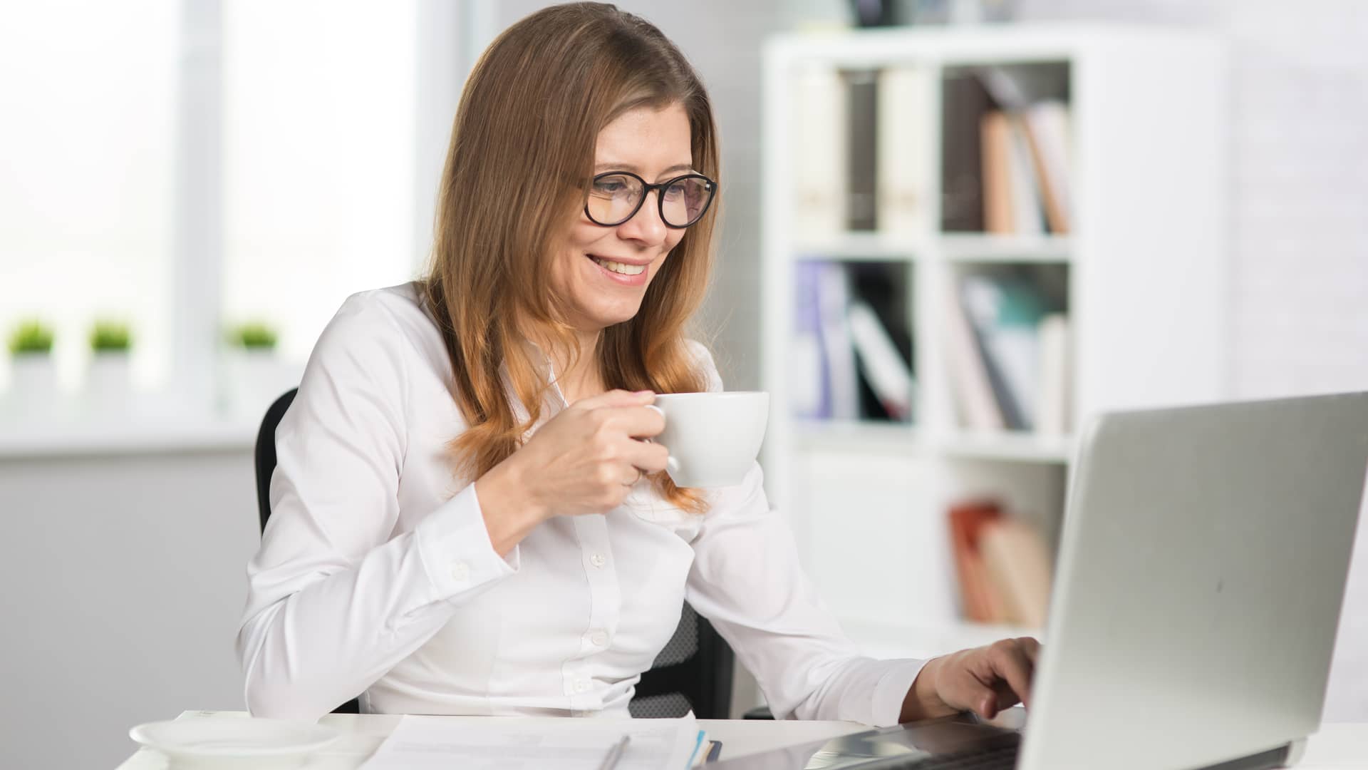 Mujer sonríe mientras toma una taza de café y navega por internet en su portátil gracias a su tarifa de R