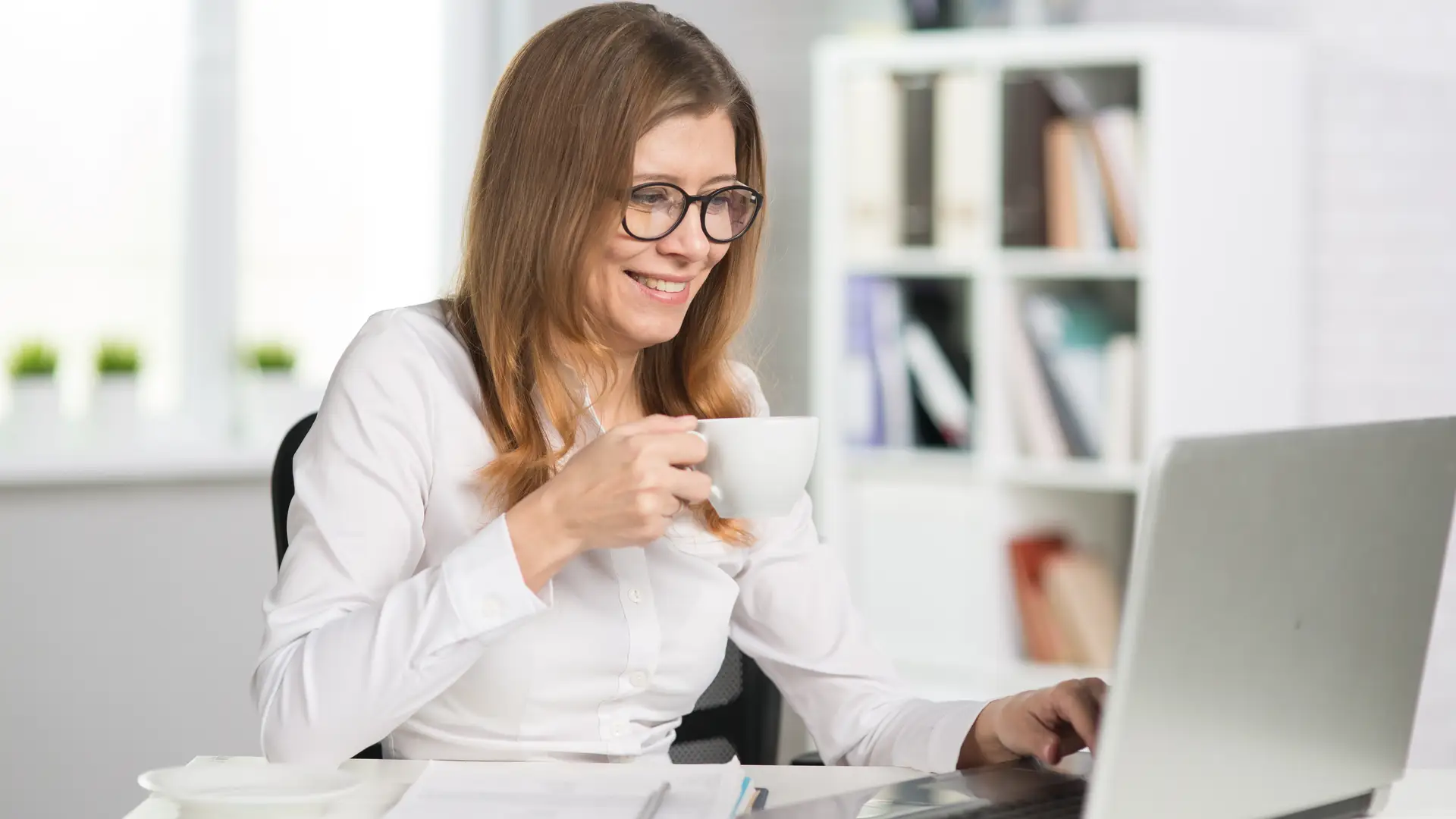 Mujer toma un café mientras teletrabaja en su portátil gracias a su tarifa de fibra de R Mujer toma un café mientras teletrabaja en su portátil gracias a su tarifa de fibra de R