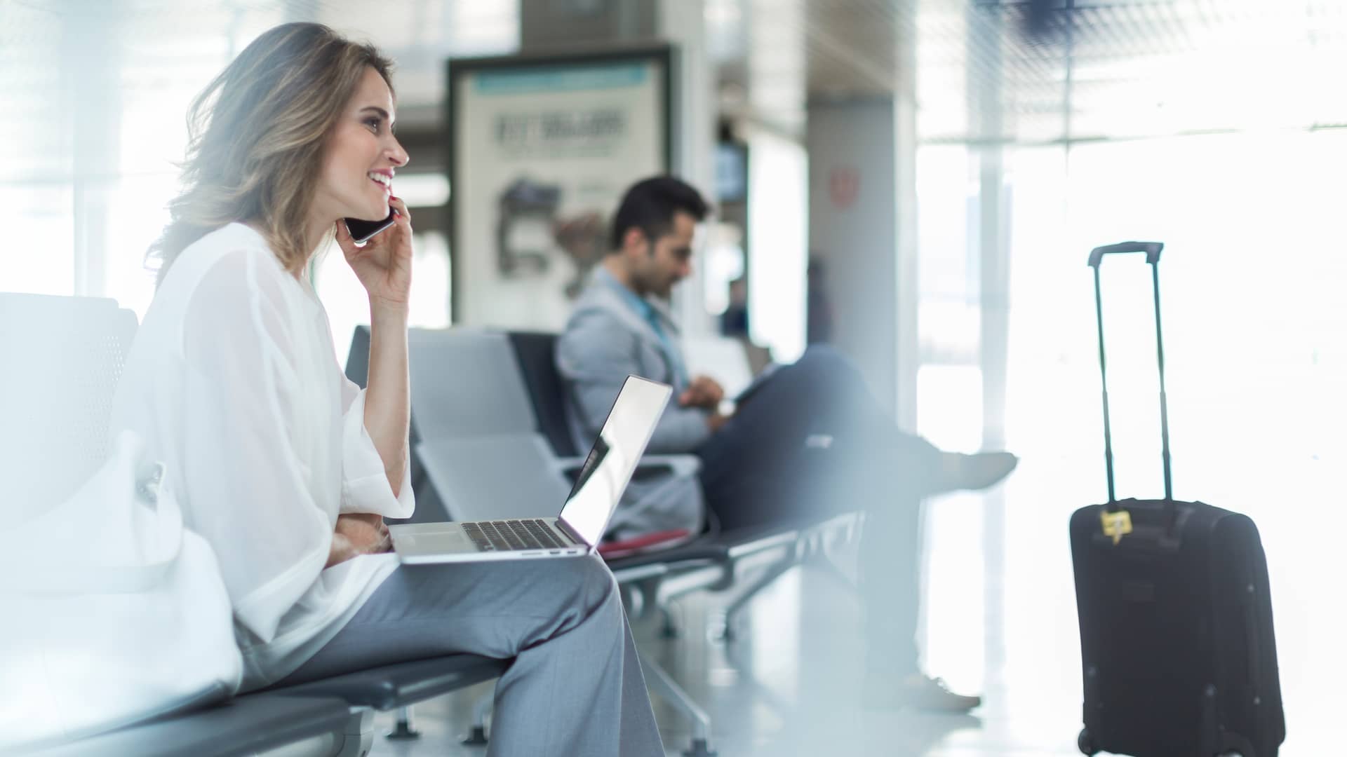 Empresaria en aeropuerto hablando por teléfono mientras sostiene su laptop simboliza llamadas internacionales