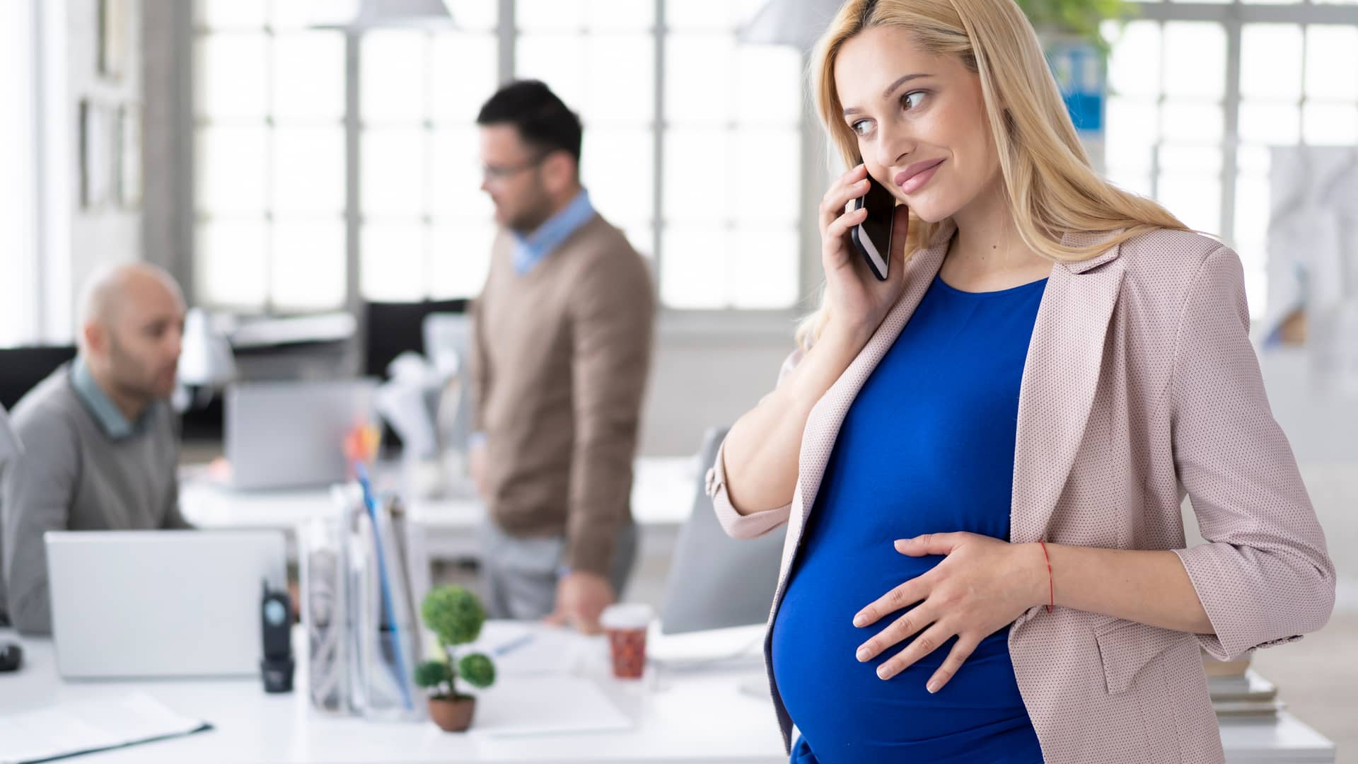 Mujer embarazada sonriente hablando en el teléfono inteligente en el lugar de trabajo representa líneas adicionales o2