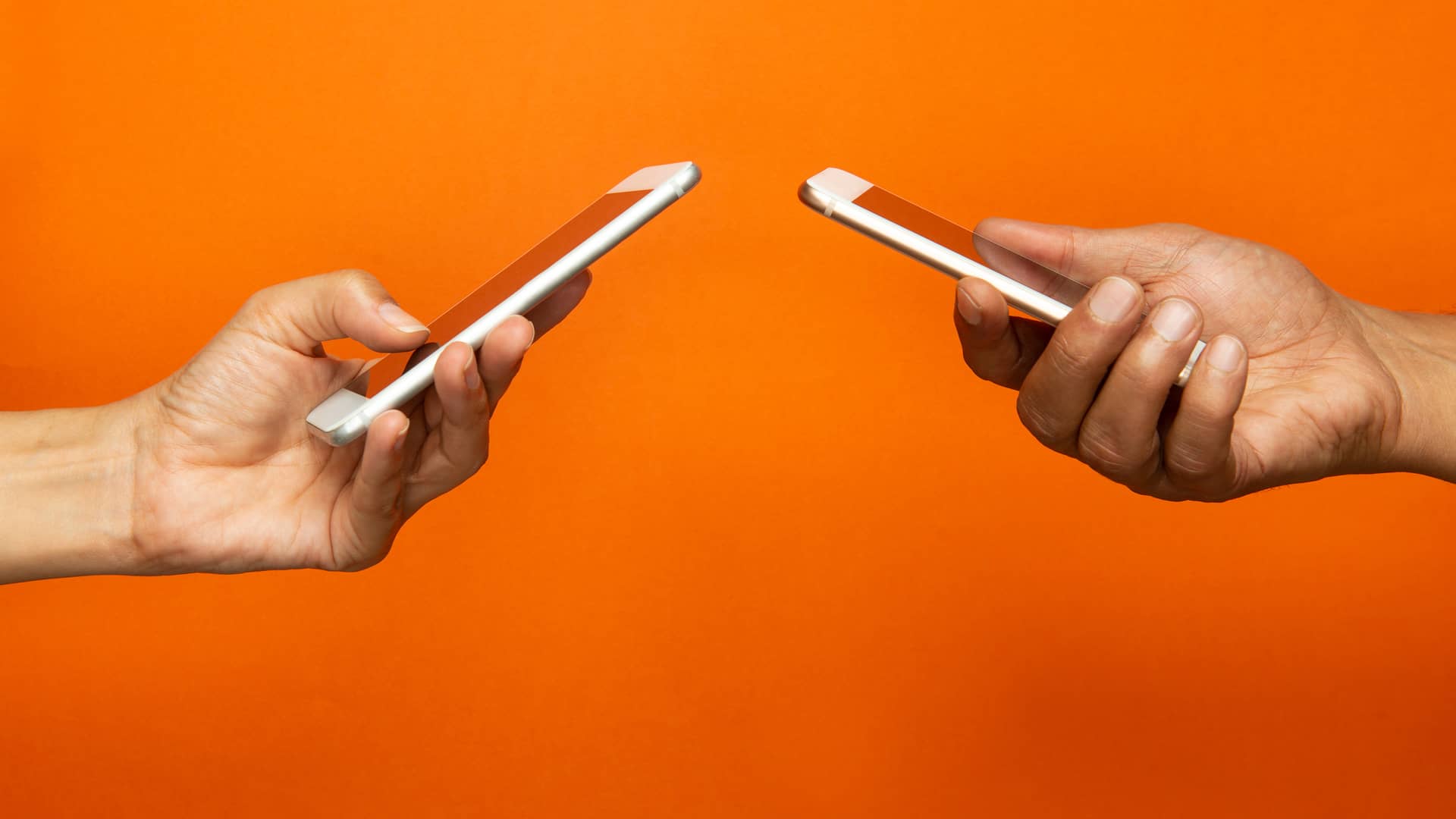 Dos manos sosteniendo teléfonos móviles compartiendo datos uno a otro