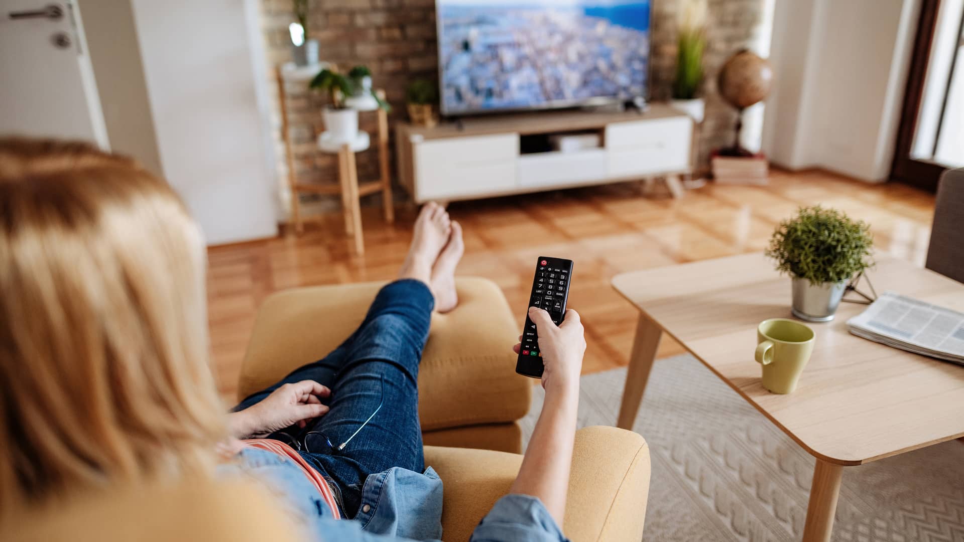Mujer descalza relajándose en casa y viendo la televisión de orange tv