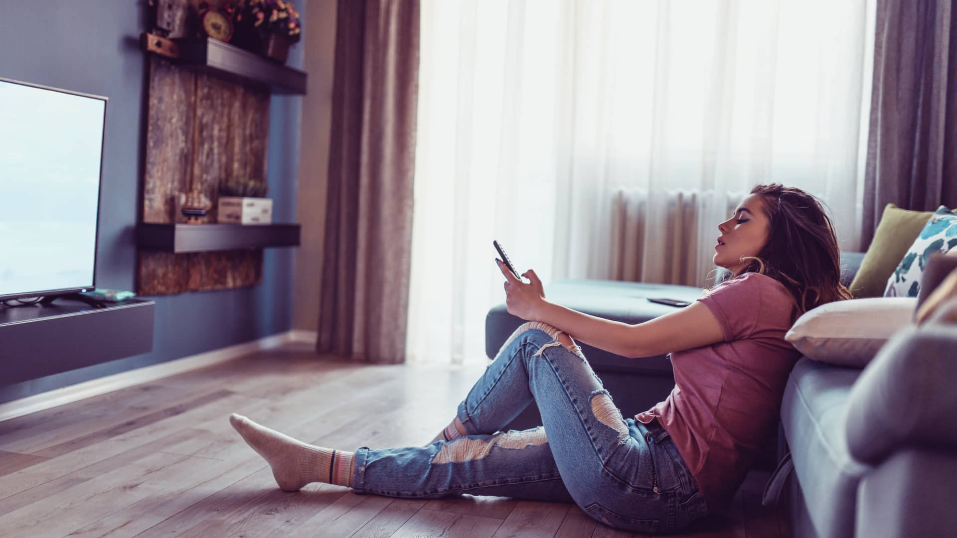 Mujer joven sentada en el suelo cambiando de canal en su smart tv, disfruta de una tarifa de pepephone de móvil y televisión