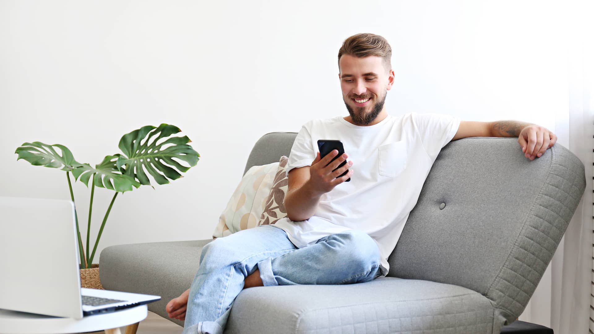 Joven sentado en el sofa usando su smartphone representa tarifas ptvtelecom