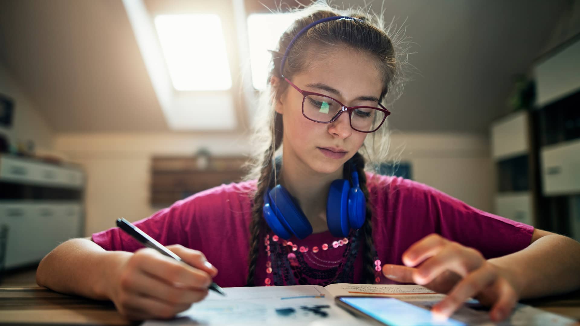Adolescente consultando el saldo de su samrtphone mientras hace los deberes