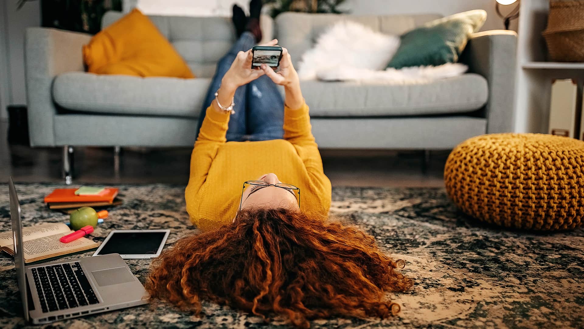 Mujer tumbada en el suelo usando su smartphone y con laptop y otros dispositivos eléctricos simbolizan móvil e internet de suop