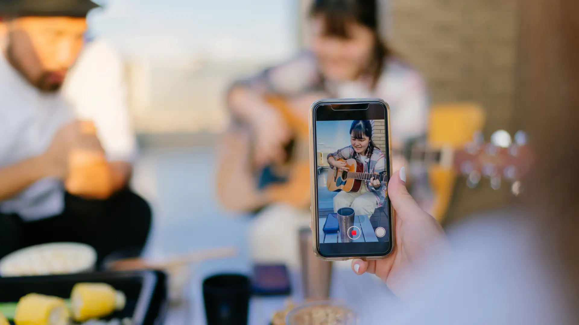 Persona grabando a chica tocar la guitarra con su smartphone simboliza móviles telecable Persona grabando a chica tocar la guitarra con su smartphone simboliza móviles telecable
