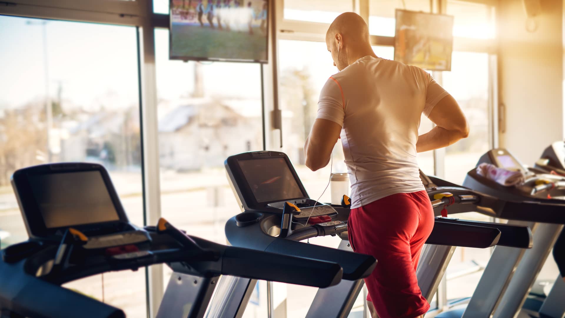 Hombre se entrena en una cienta de correr en un gimnasio cuyas televisiones disfrutan del servicio vodafone empresas de televisión para negocios