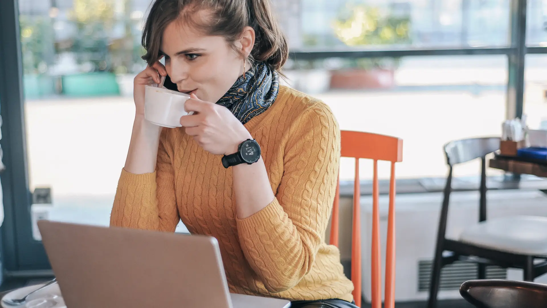 Joven tomando un café y trabajando mientras se encuentra en una llamada en espera